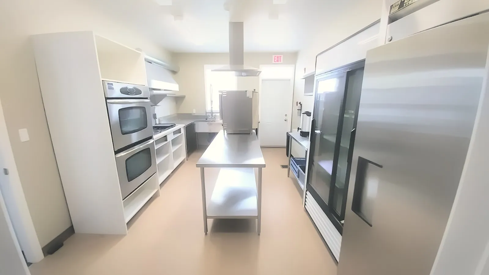Commercial kitchen with stainless steel ovens, prep table and fridges
